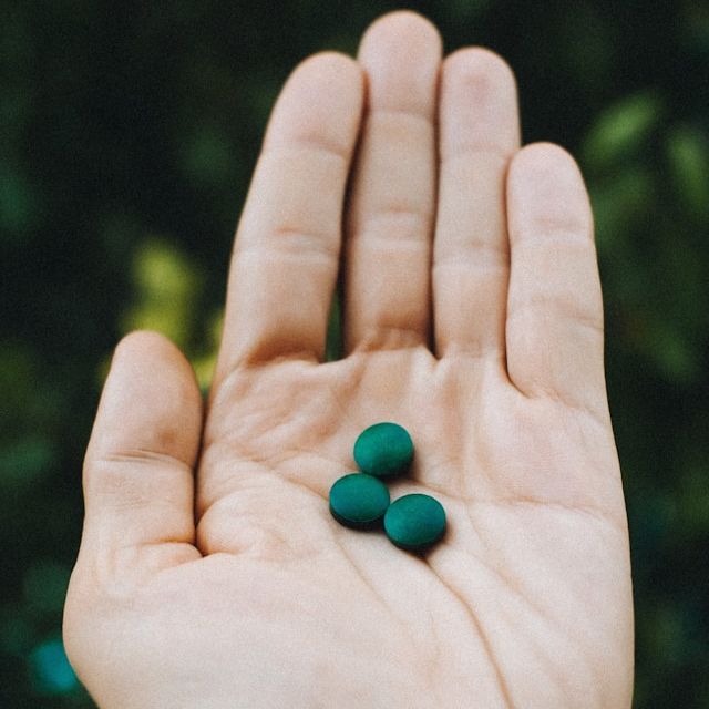 Hand holding three green pills.