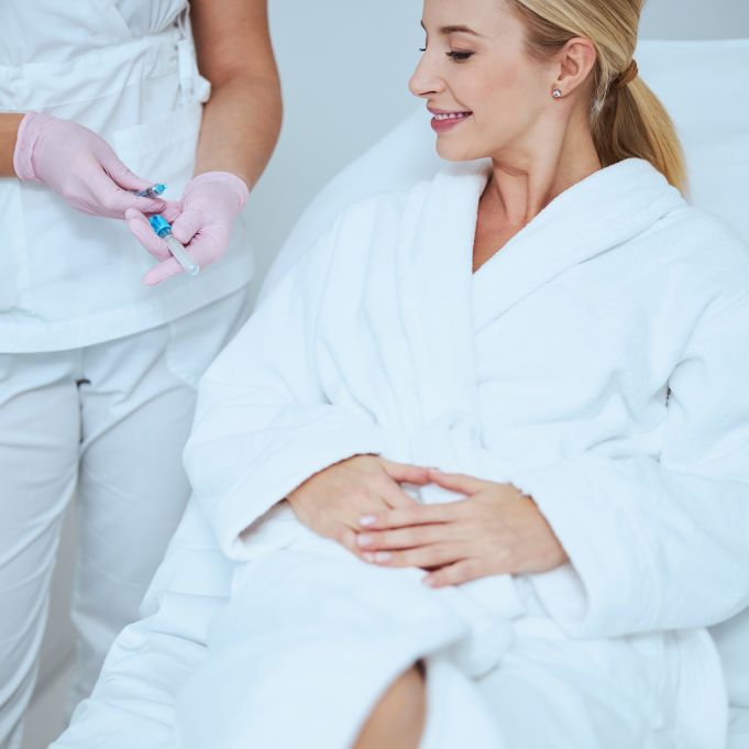 Female doctor in latex gloves showing a disposable syringe and a glass tube to her smiling patient
